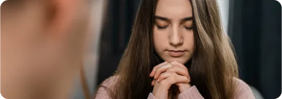 Mulher com olhos fechados e mãos postas em posição de oração.